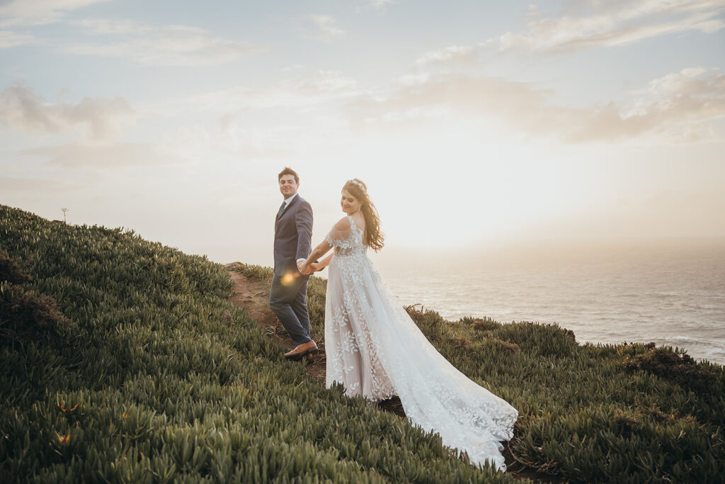 Couple holding hands on a grassy hill overlooking the ocean