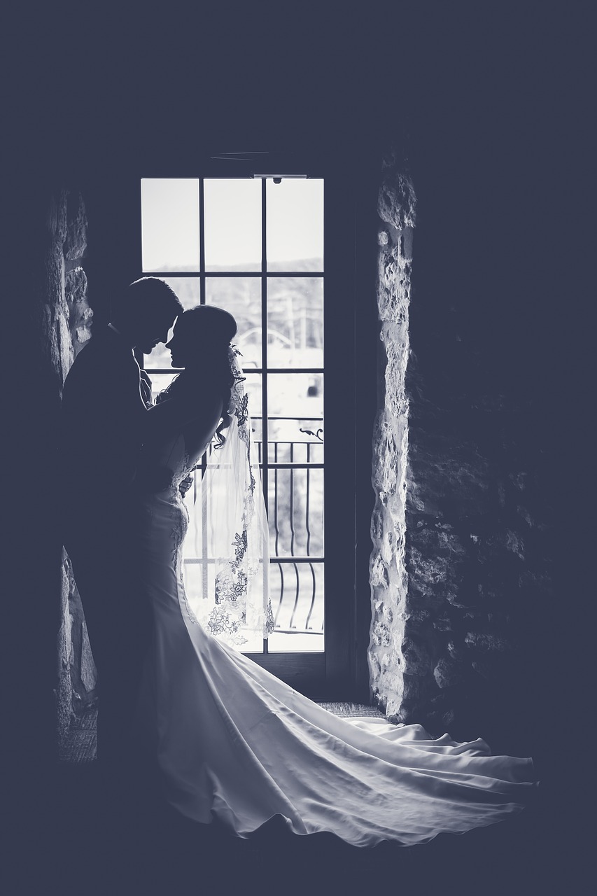 Silhouetted bride and groom embrace by a window.
