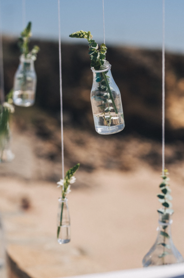 Small glass bottles with greenery hang from strings.