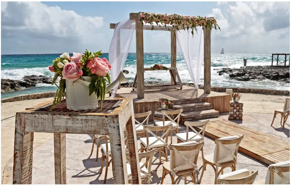 Beach wedding ceremony setup with arch, chairs, flowers