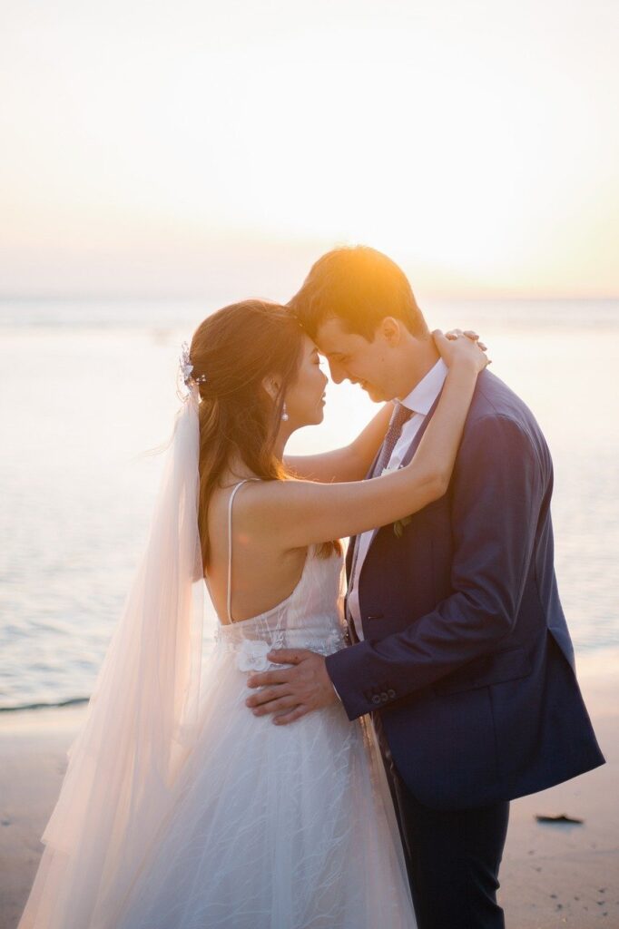 Bride and groom embrace on a beach at sunset