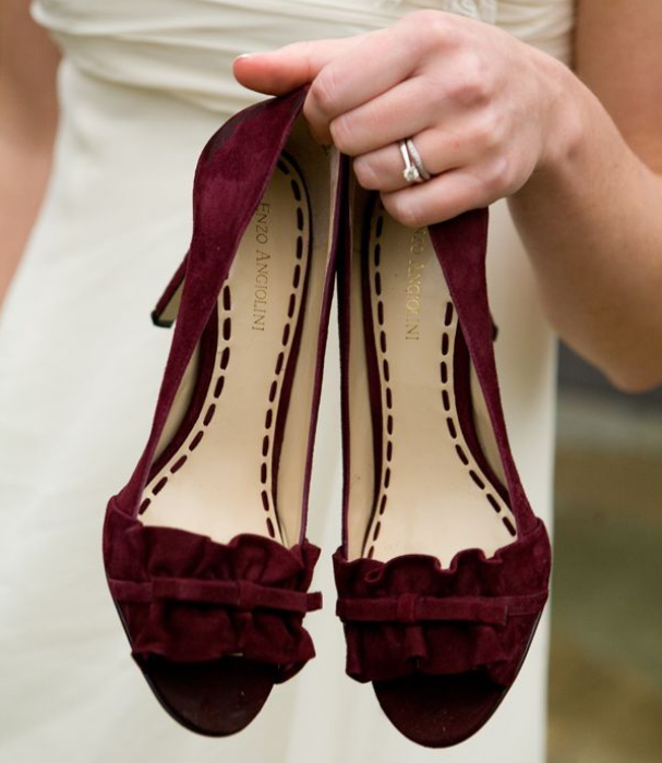 Woman holding burgundy suede shoes with ruffles and bows