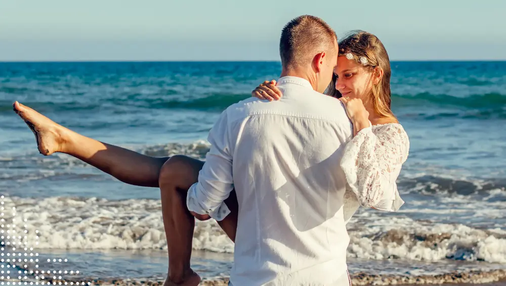 Man carrying woman on beach, ocean in background