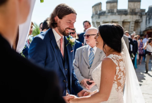 Groom in blue suit, bride in white lace dress holding hands