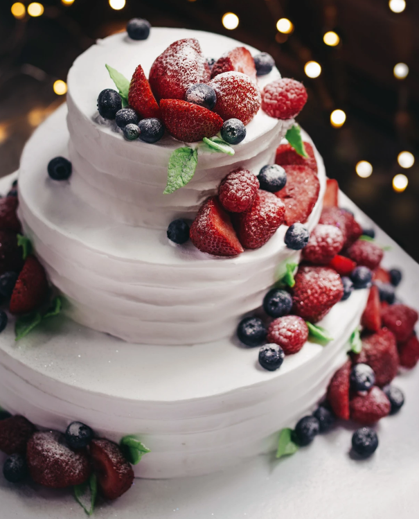 Three-tiered white cake with berries and powdered sugar.