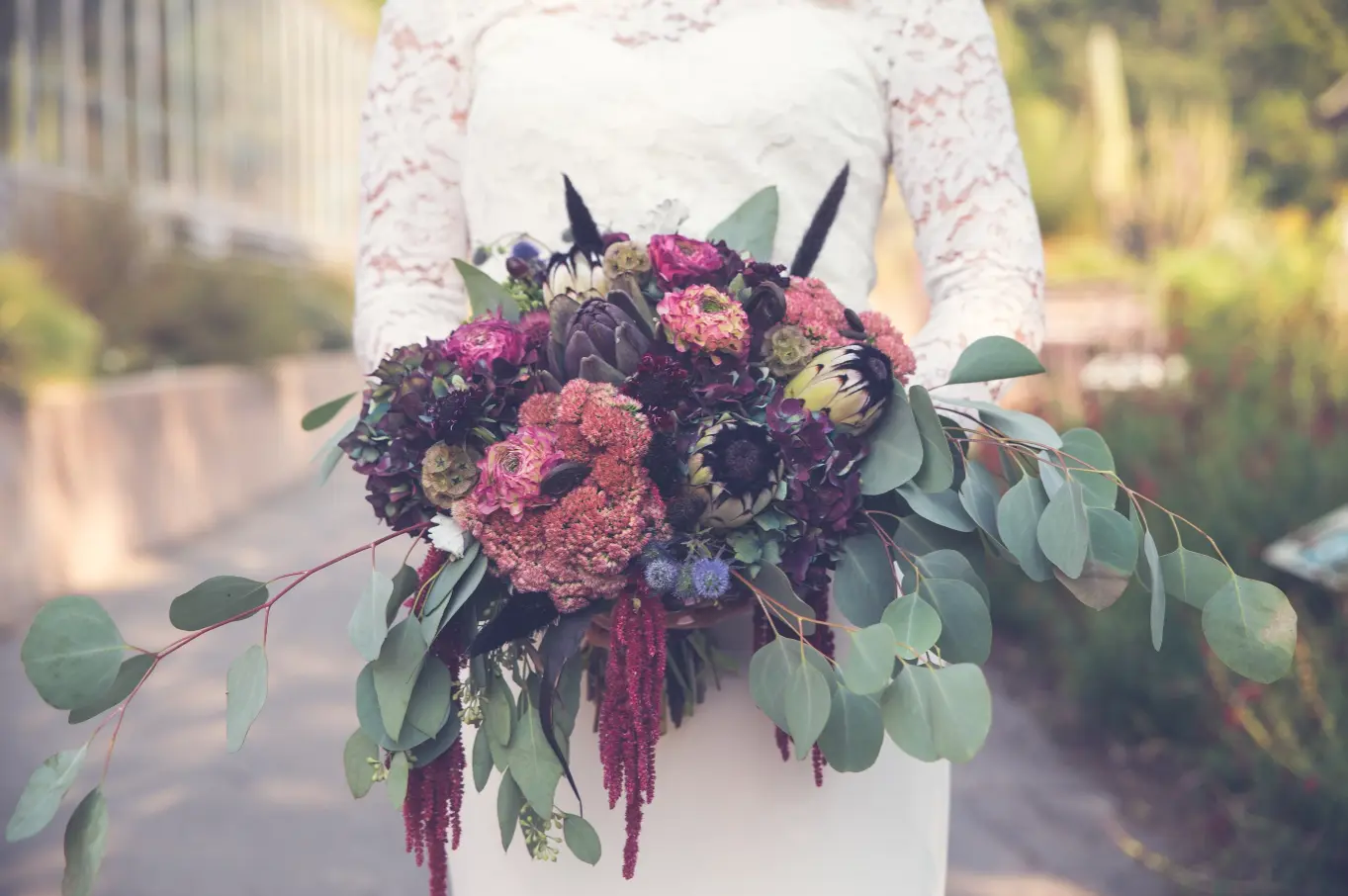 Bride in white lace dress holding a dark floral bouquet.