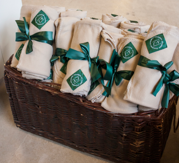 Rolled beige blankets with green ribbons in a wicker basket.